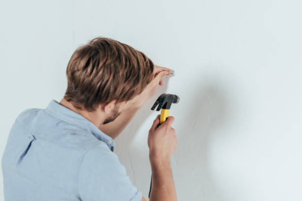 Back view of young man hammering nail in wall at home